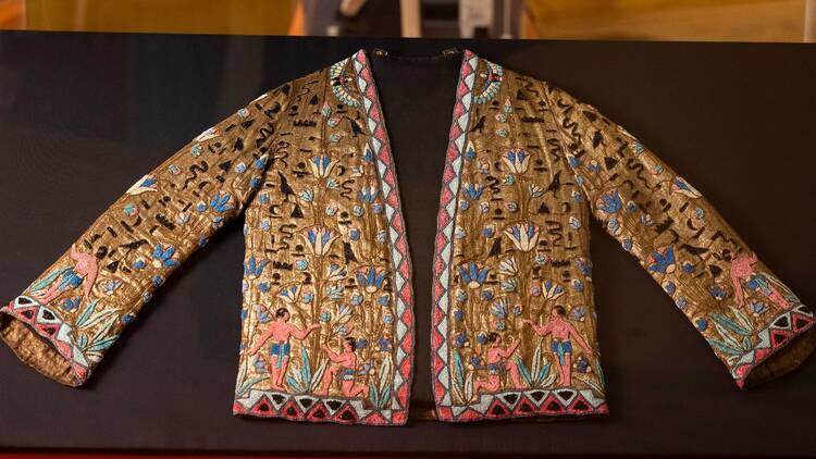 A gold lame jacket intricately decorated with beads resembling heiroglyphic, and figures wearing loincloths