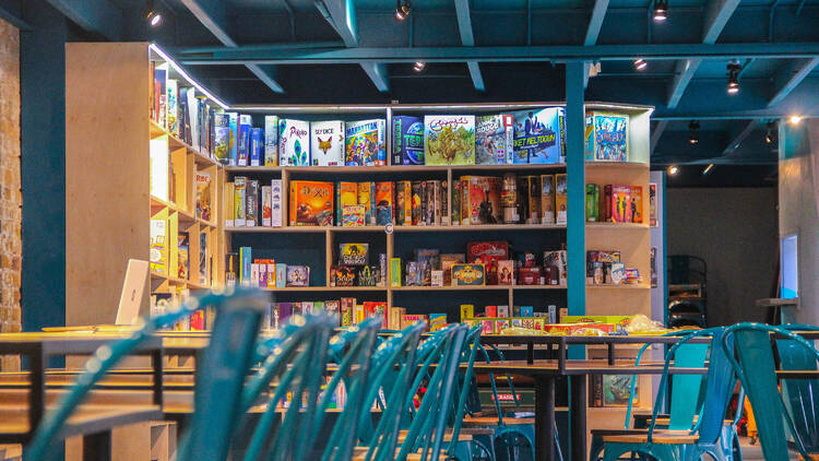 Inside board game cafe Draughts, shelves rammed with board games and lots of tables with turquoise chairs. 