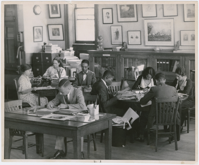 A group of people gather in a reading room in a historic photo.
