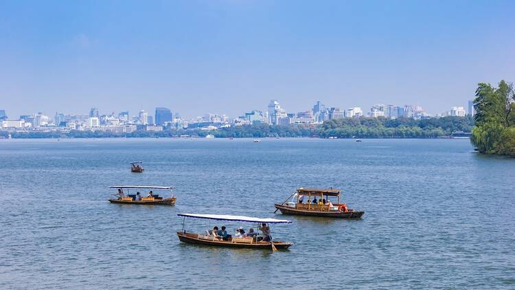 Small wooden boats on the West Lake in front of the skyline of Hangzhou, China