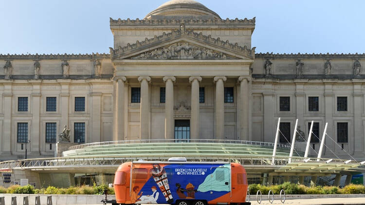 The outside of the Brooklyn Museum with a trailer out front reading Brooklyn Museum on Wheels.