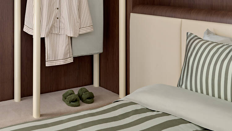 A bed with striped green bedding and a pair of pajamas hanging. 