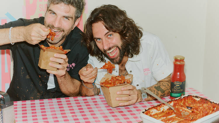 Two men eating pasta at a table.