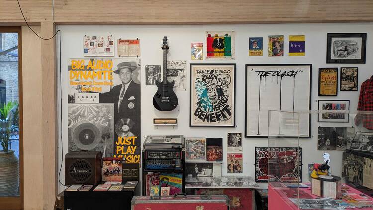 A wall display of The Clash and Big Audio Dynamite posters with a black electric guitar in the middle