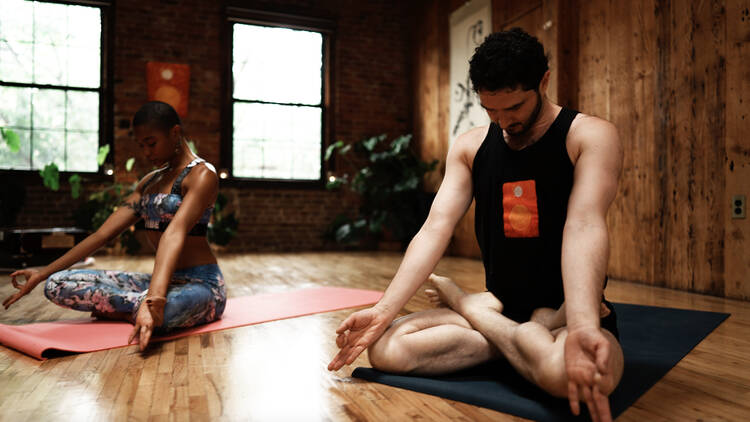 Two people sit with crossed legs on yoga mets while meditating.