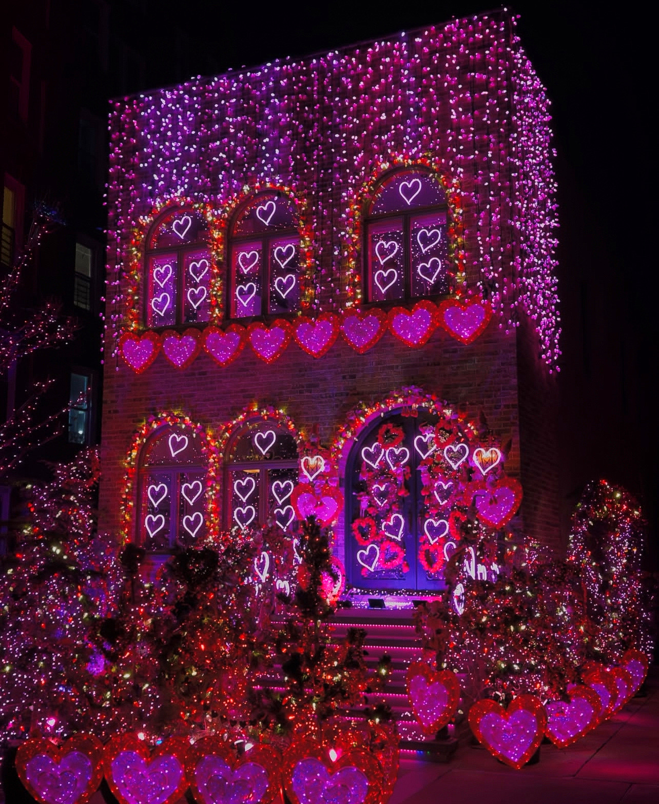 A two-story brick home is decorated with pink decor for Valentine's Day.