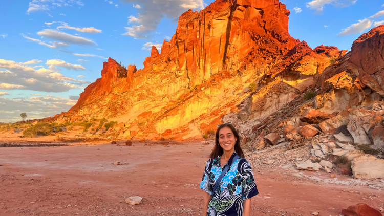 Girl in blue shirt standing in front of large red rock in desert