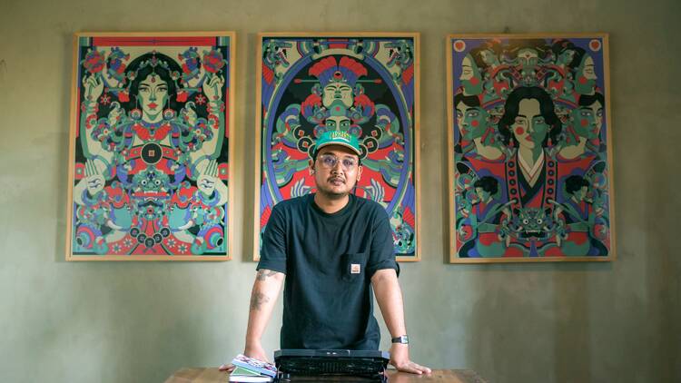 Balinese illustrator Cokorda Martin in his workspace, in front of three of his art prints