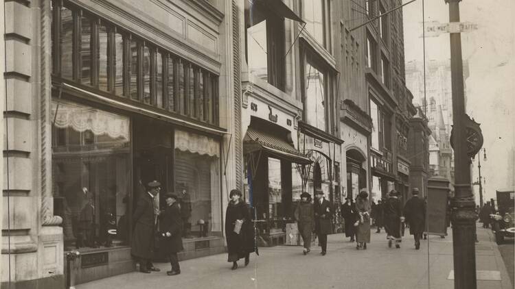 People in dark, formal clothing walk along Fifth Avenue.