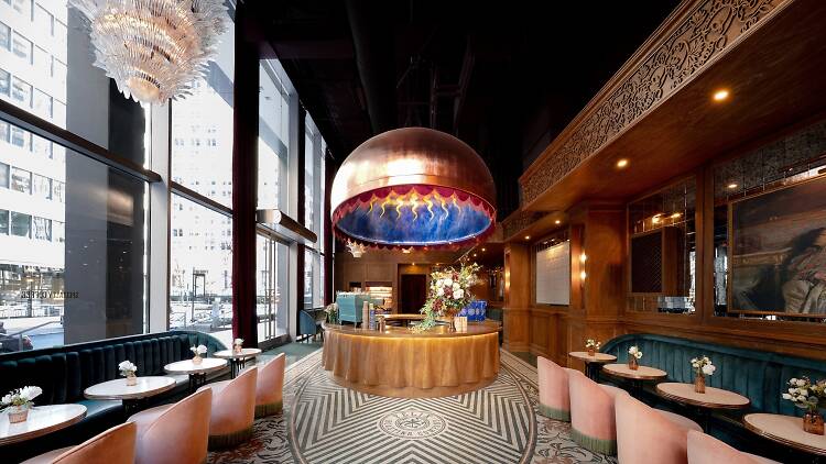 Interior of Felix Roasting Co. with a black and white flooring, pink velvet swivel chairs and blue velvet booths. The center of the image is a large copper dome over looking the cafe counter