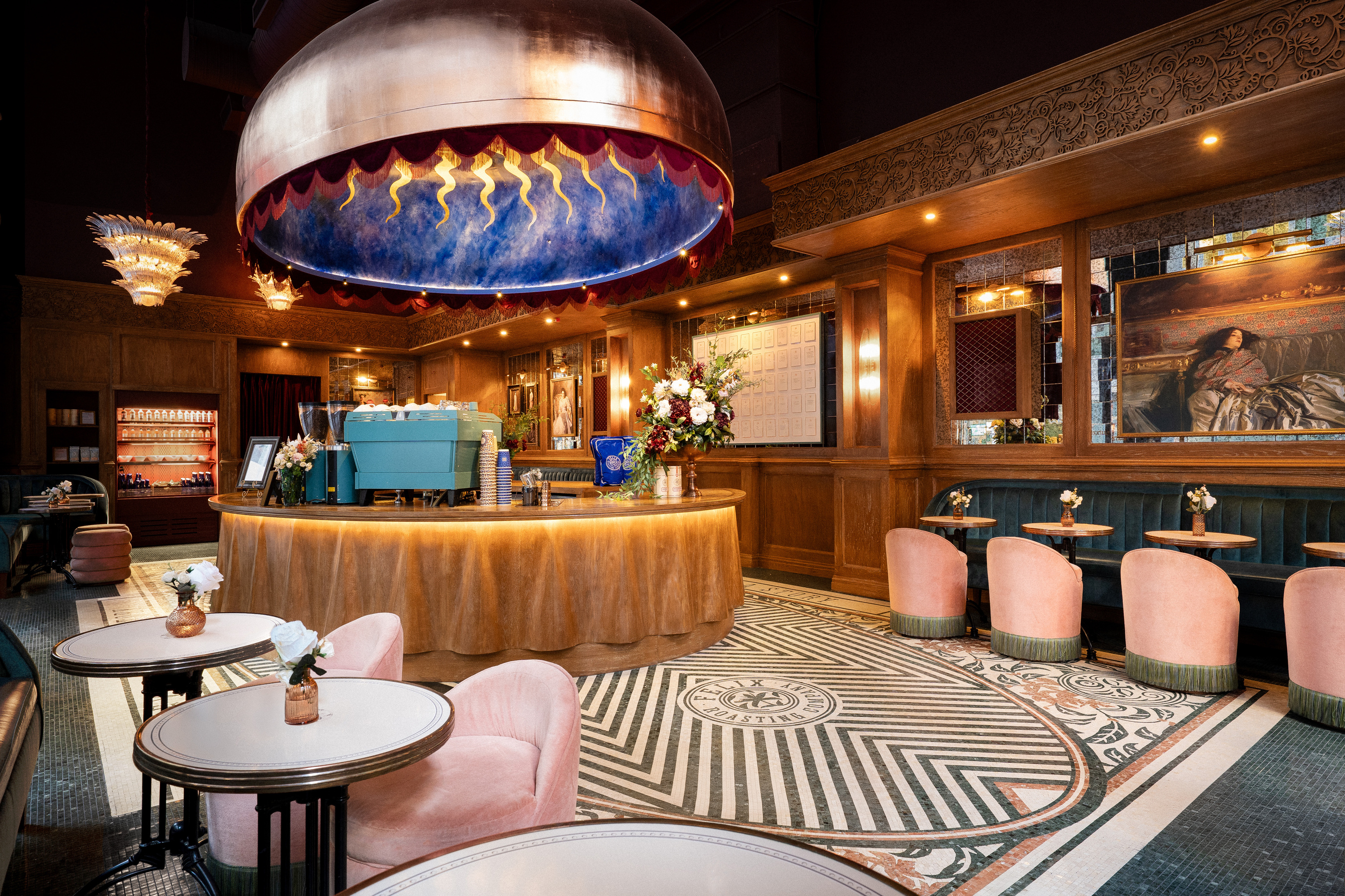 Interior of Felix Roasting Co. with a black and white flooring, pink velvet swivel chairs and blue velvet booths. The center of the image is a large copper dome over looking the cafe counter