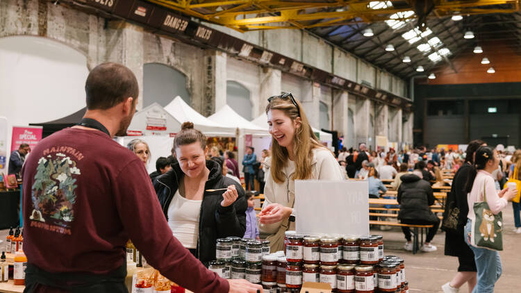 People at a market stall looking at a product in jars. 