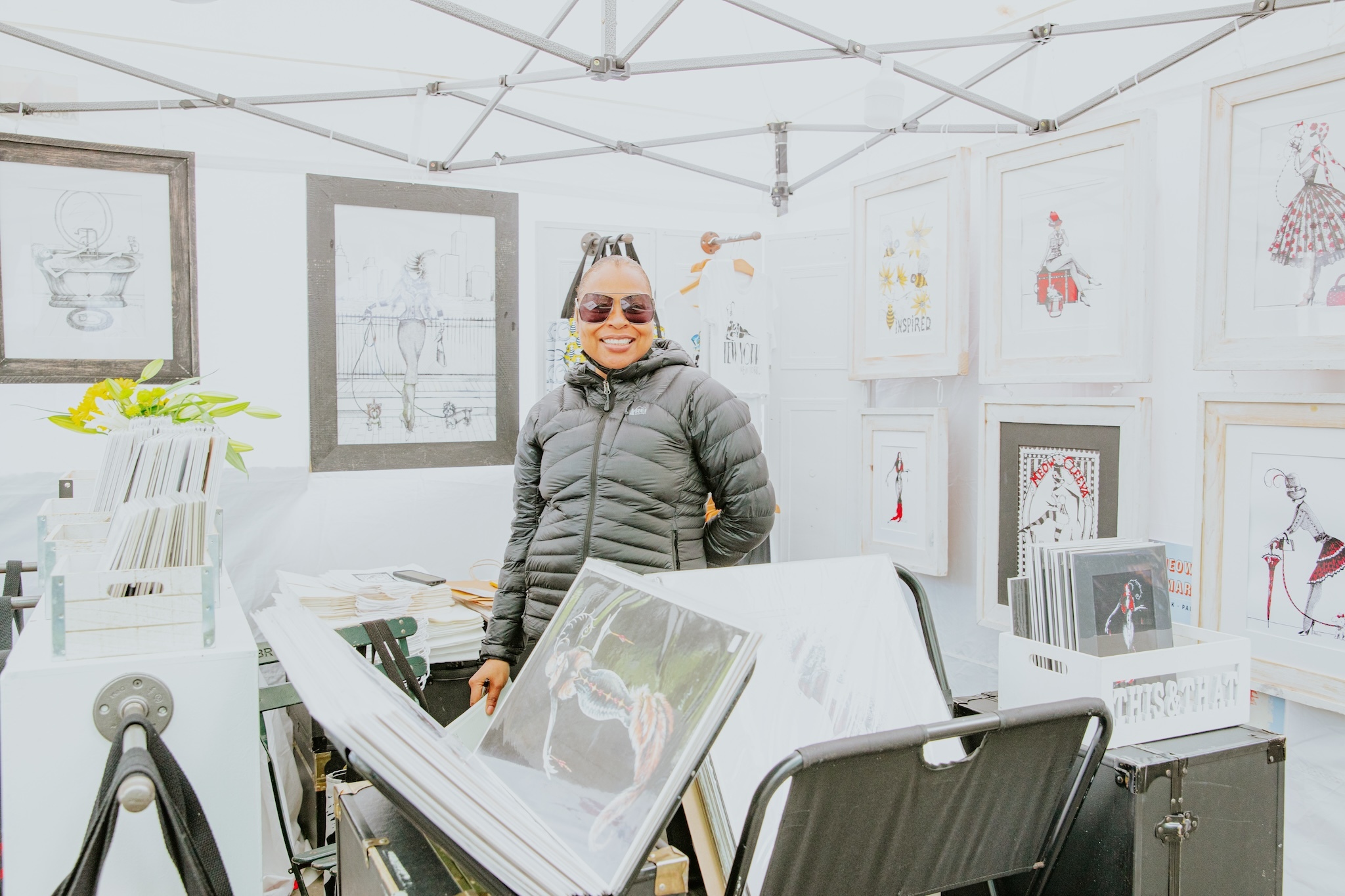A woman stands in the middle of a booth with artwork.