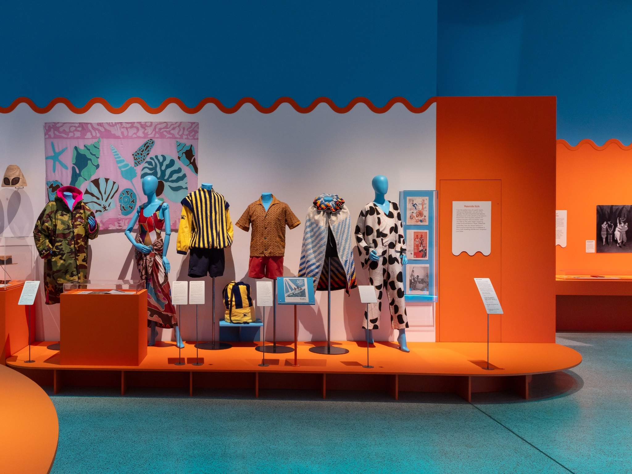 A row of mannequins wearing beach outfits stand on an orange platform