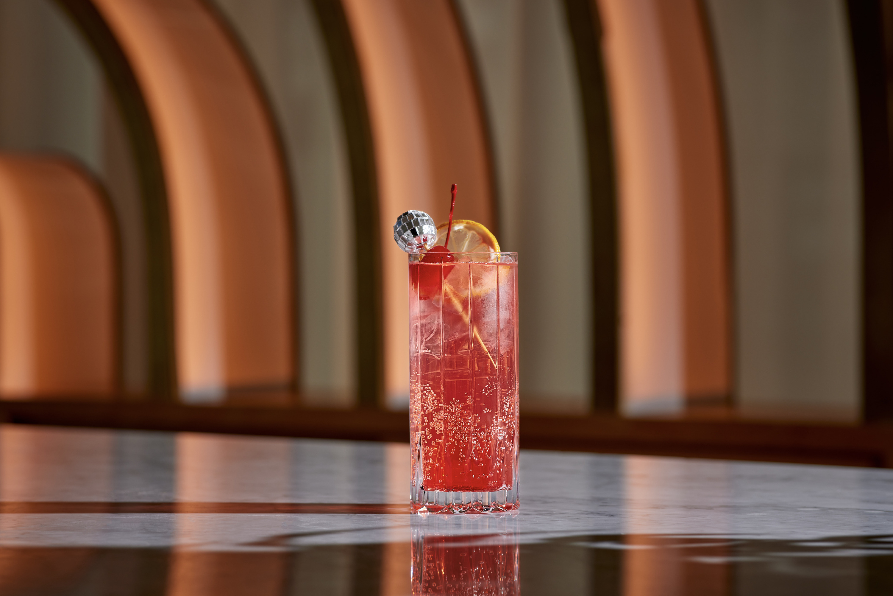 Boys just want to have fun cocktail at Virgin Hotels, is a red drink in a highball glass with a little disco ball toothpick in it