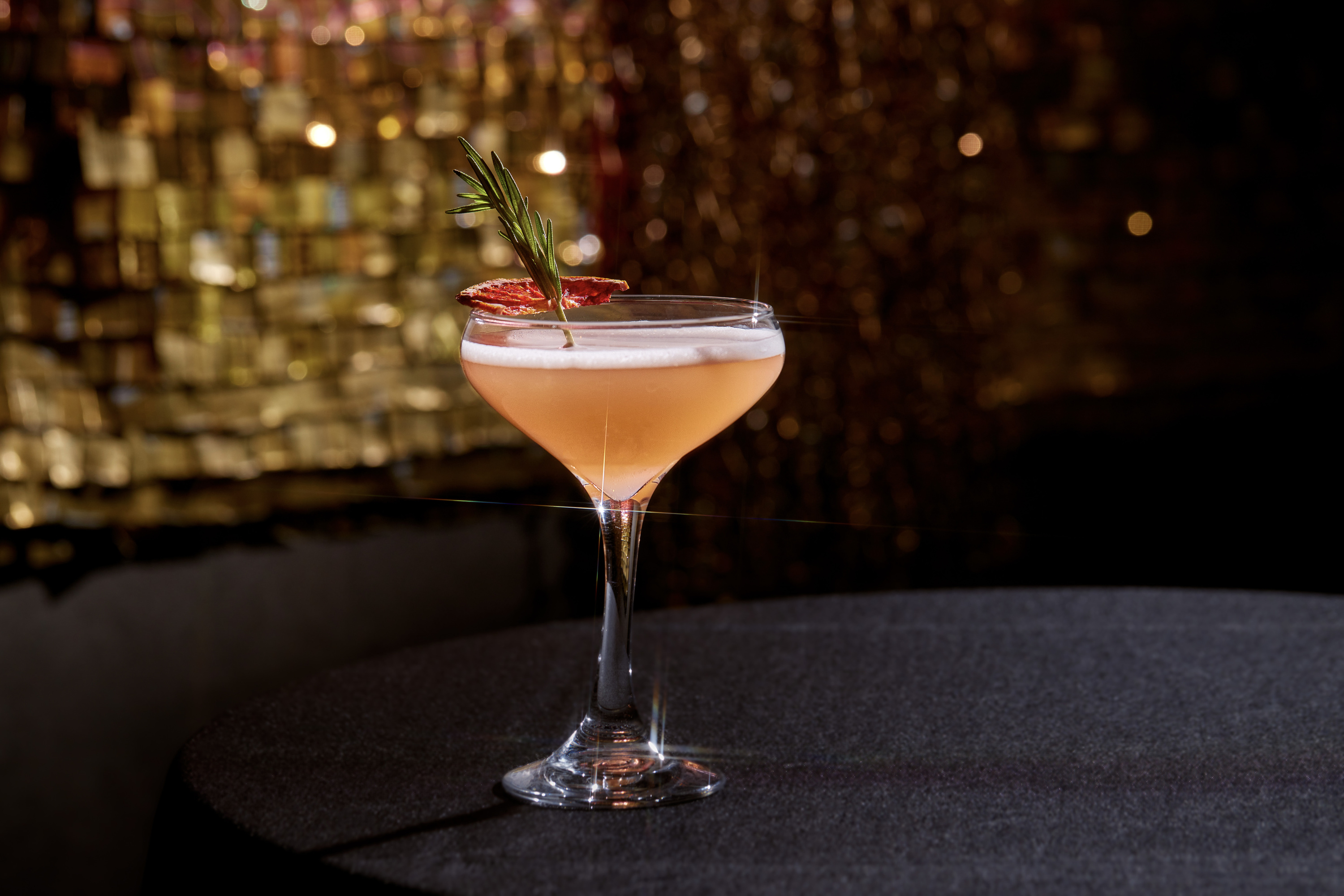 She’s throwing shade cocktail at Virgin Hotels is a peachy color drink in a coupe glass and a sprig of thyme