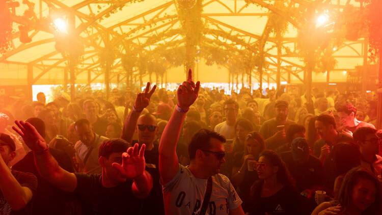 A crowd of people dancing inside a large tent at Between the Bridges