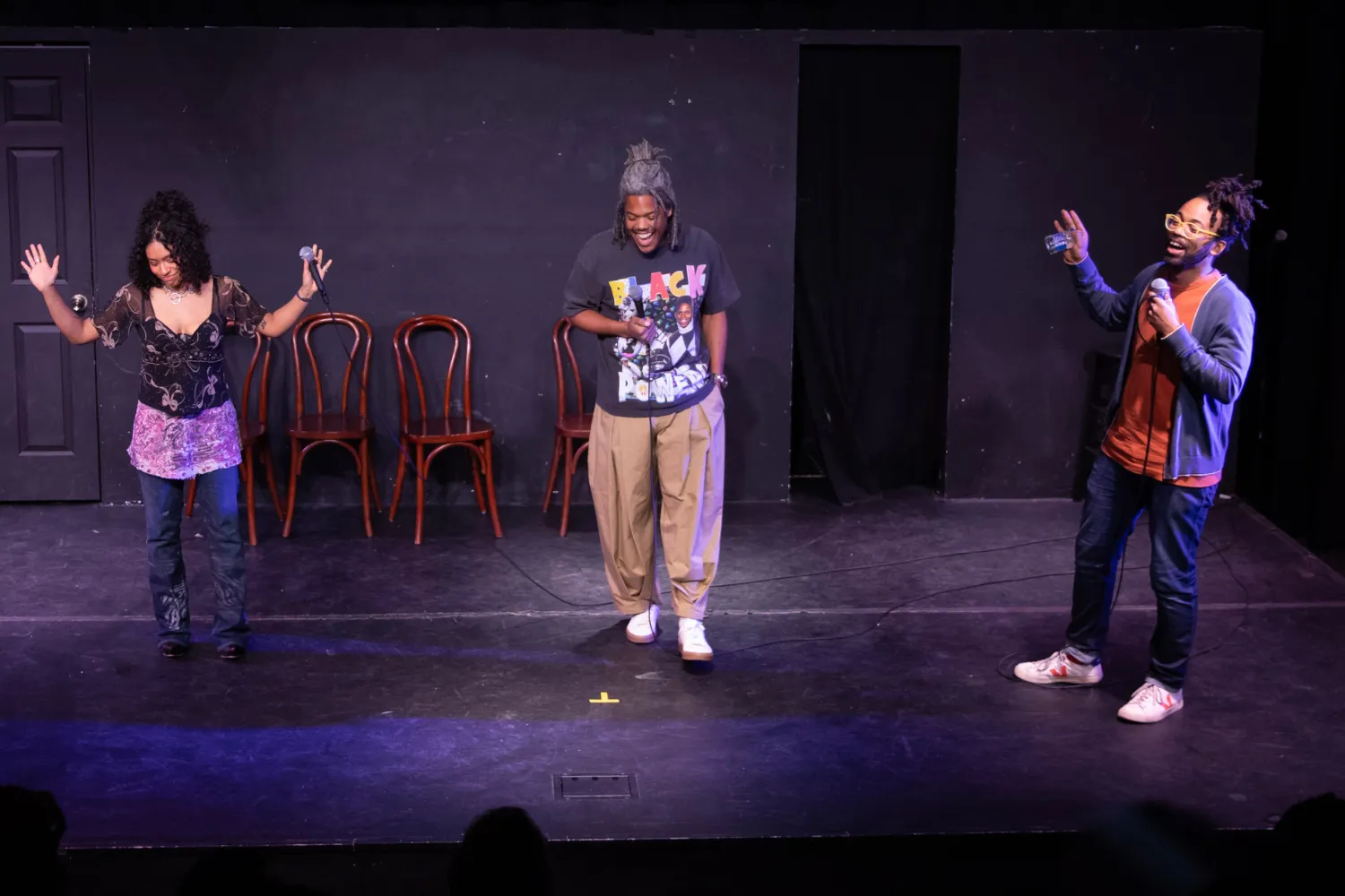 Three performers stand on stage with a microphone.