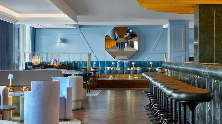 Empty Lyaness bar showing powder blue banquette seating, parquet floor and black stools lined up by green marble bar