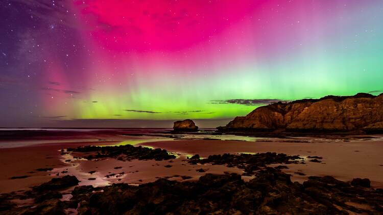 Aurora Australis over a rocky beach under a purple sky