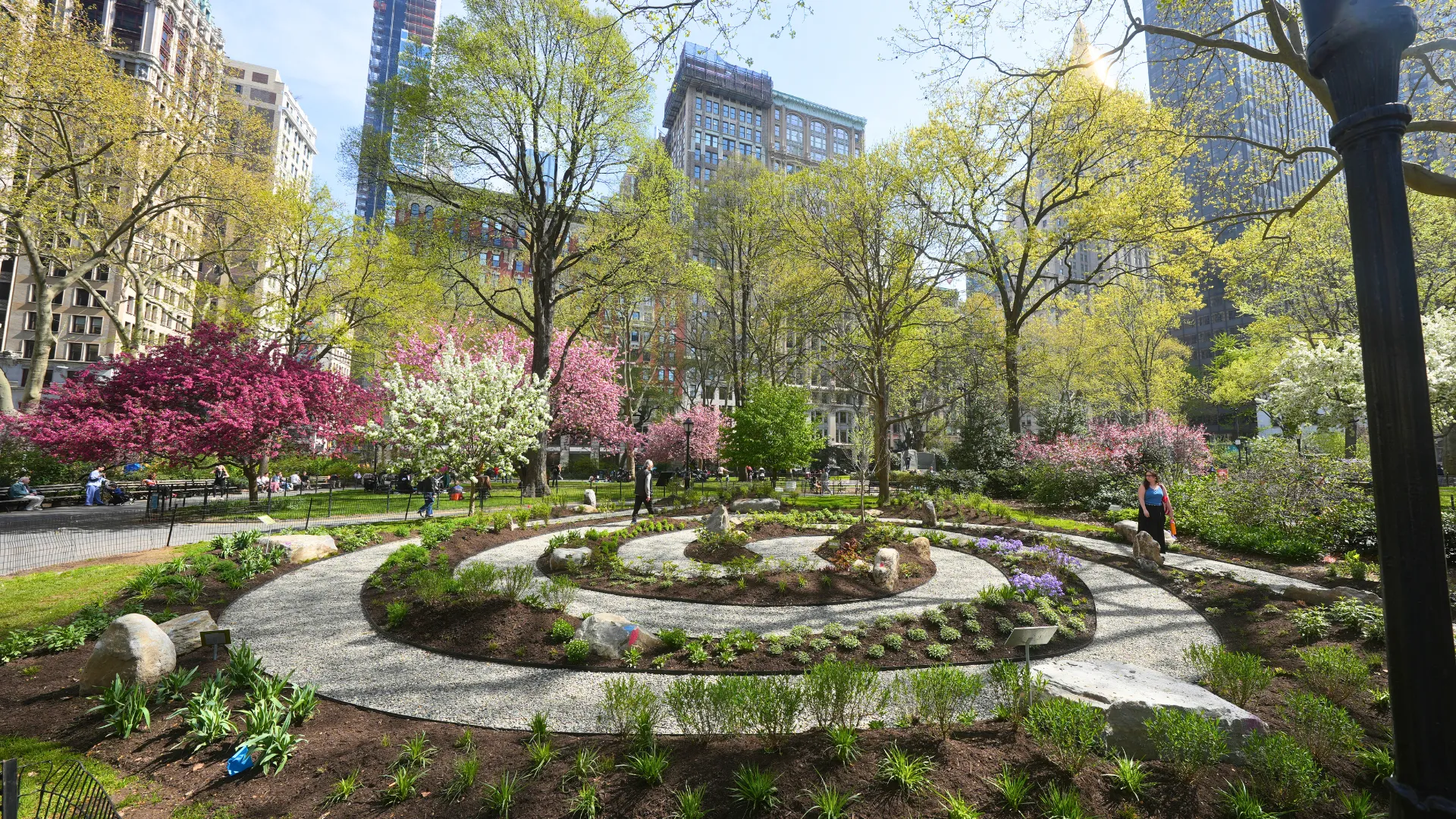 A spiral pathway inside of a park with blooming flowers and trees.