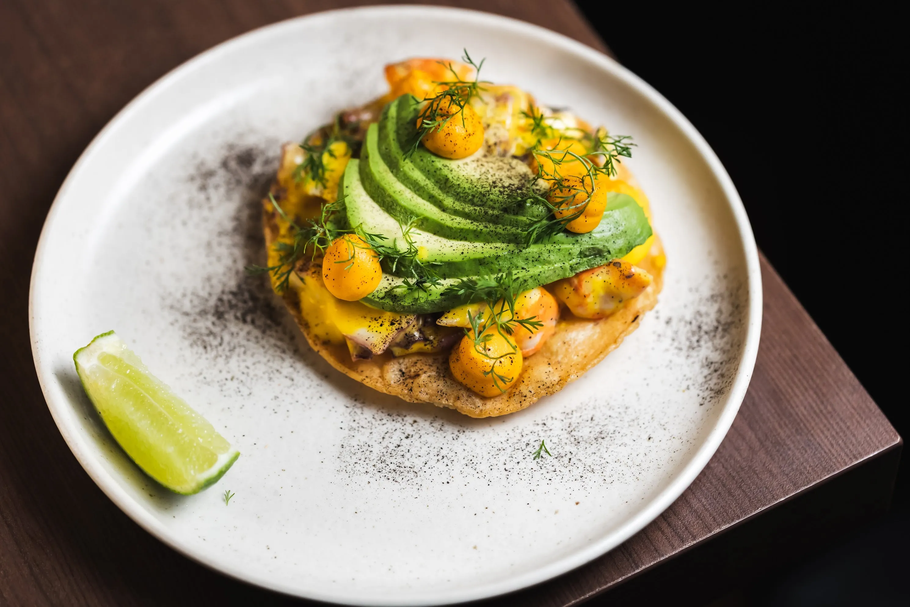 A tostada with avocados and seafood and a wedge of lime
