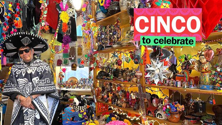 A mani n a traditional Mexican outfit stands inside a Mexican folk art store, which is packed with trinkets.
