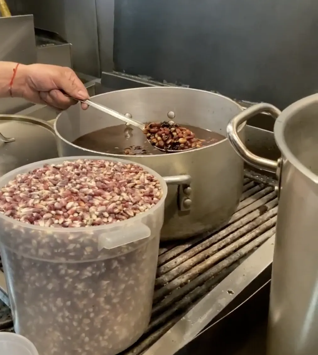 | A person holding a spoon of blue corn in a pot of water