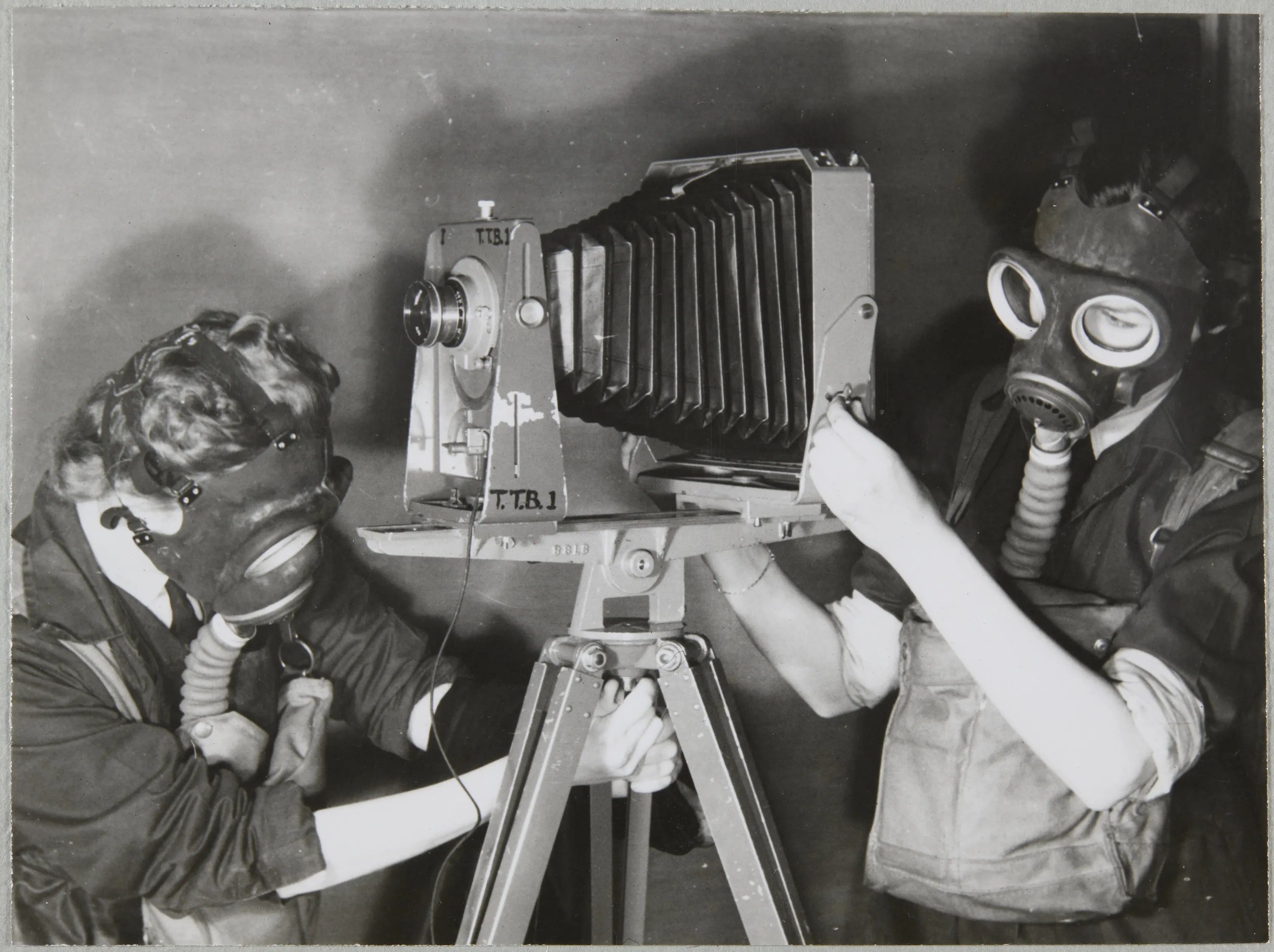 Two Women's Auxiliary Air Force (WAAF) trainees practising photography wearing gas masks