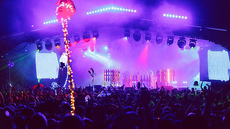 A crowd of people in front of a colourfully lit stage. 