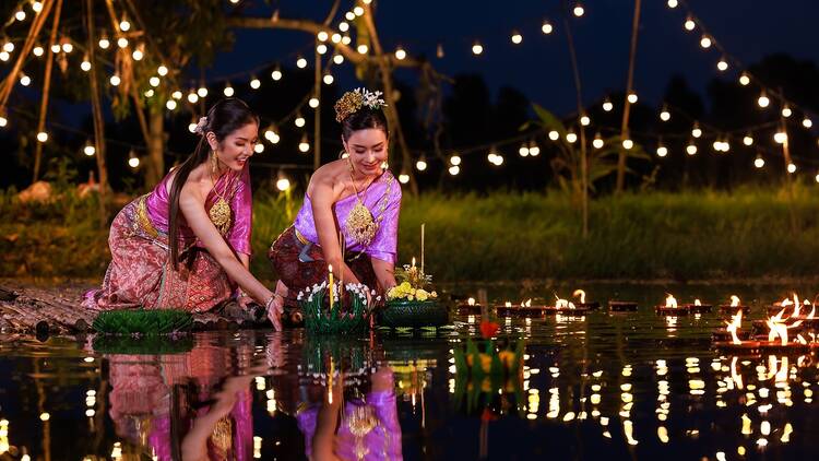 Loi Krathong Festival, Two thai woman holding a krathong sitting on a raft by the river, Asian women in traditional Thai costumes bring krathongs to float on Loi Krathong Day, traditions and culture of Thailand,