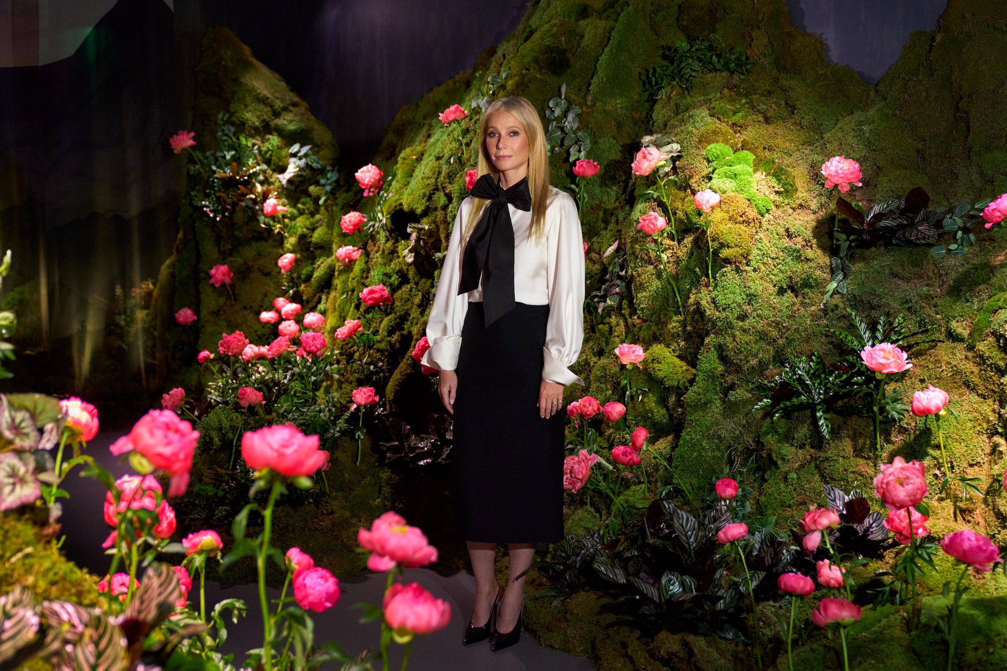 Gwyneth Paltrow, a white blond woman, looks up at an immersive floral exhibit.
