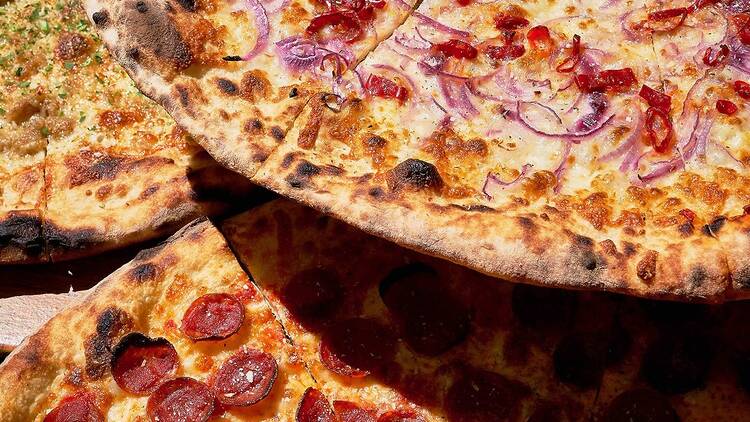 Three whole pizzas with onions and pepperoni toppings