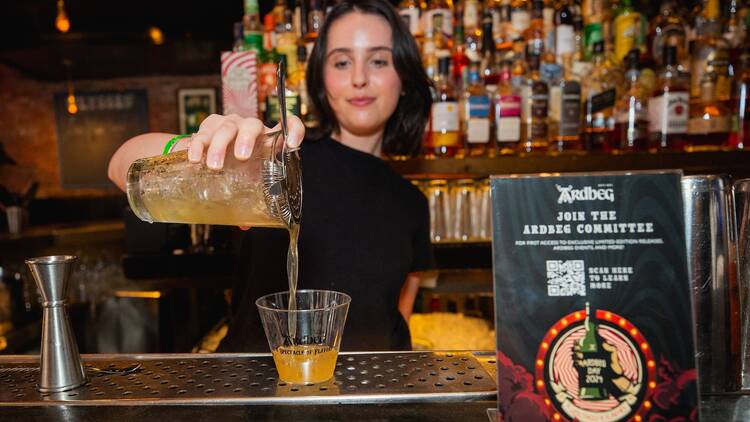A woman pours a drink into a cup from a shaker.