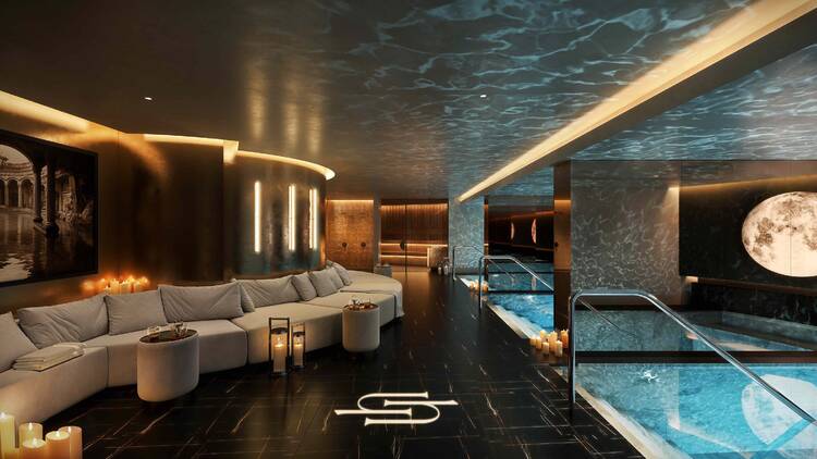 A room with swimming pools and a wall lined with couches. 
