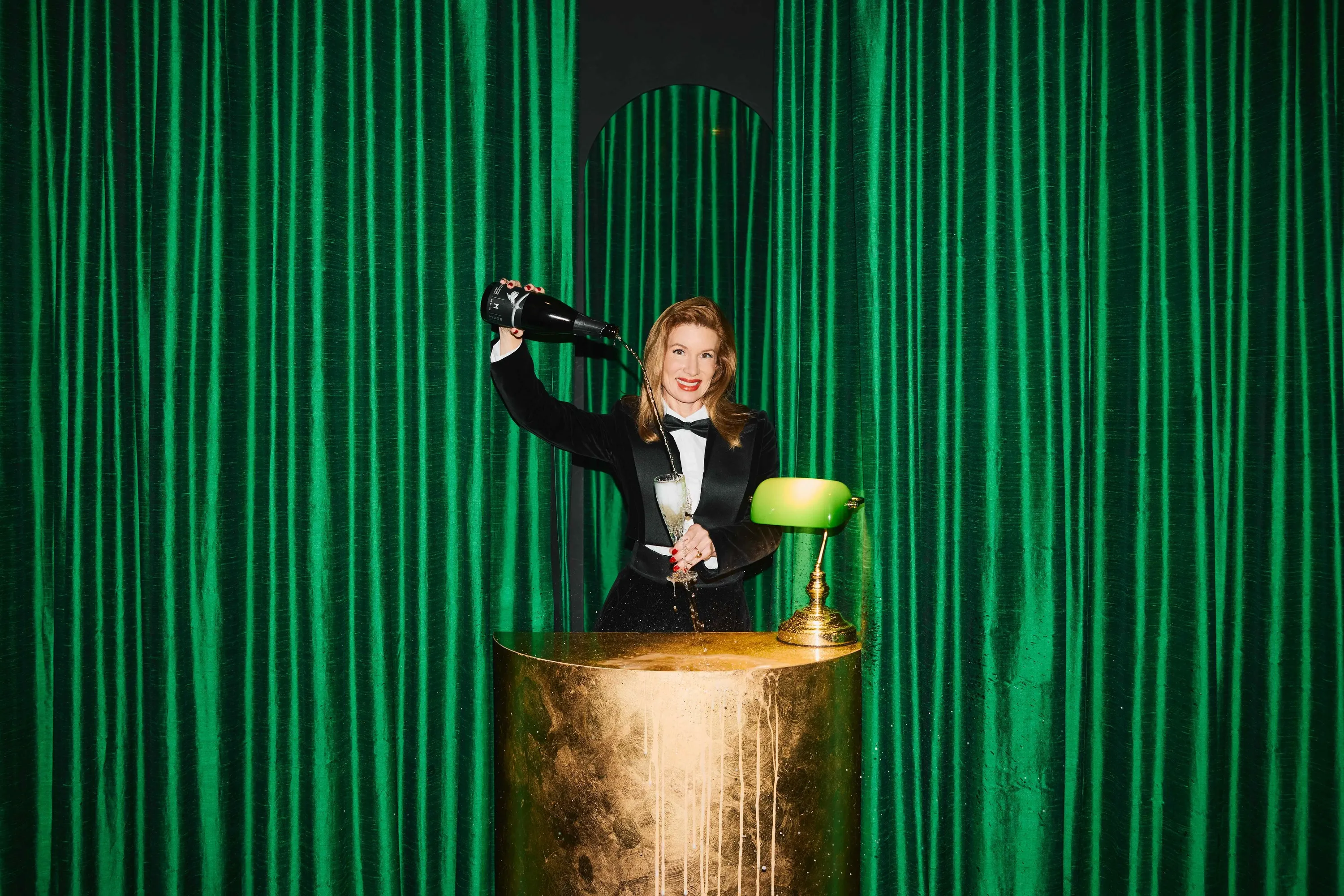 Woman pouring champagne in front of green curtain