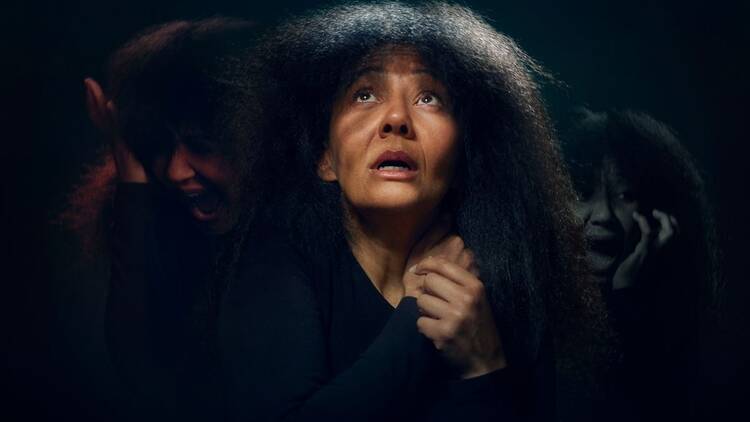A woman in front of a black background appears scared 