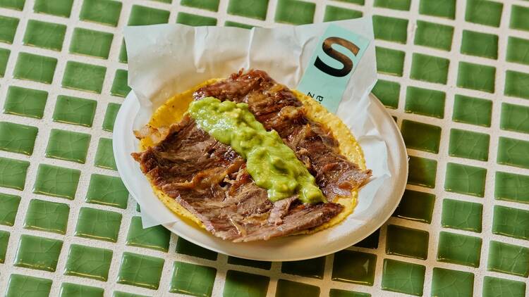 A taco with green salsa on a green and white tiled background