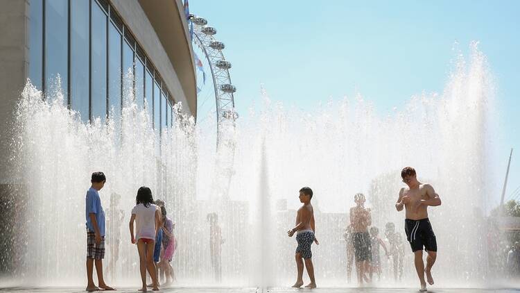 Children playing in a fountain in London with the London Eye in the background