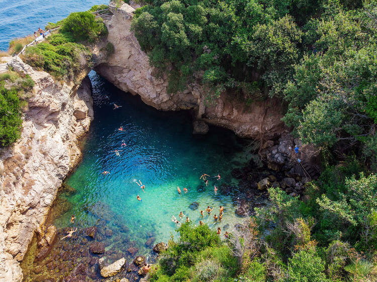 People bathing in Sorrento at Regina Giovanna Queen's bath - Tourists swimming in crystal clear blue waters of popular lagoon on Amalfi Coast. Italy