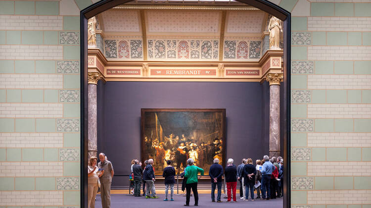 A crowd of people gather around a painting by Rembrandt displayed inside the Rijksmuseum.