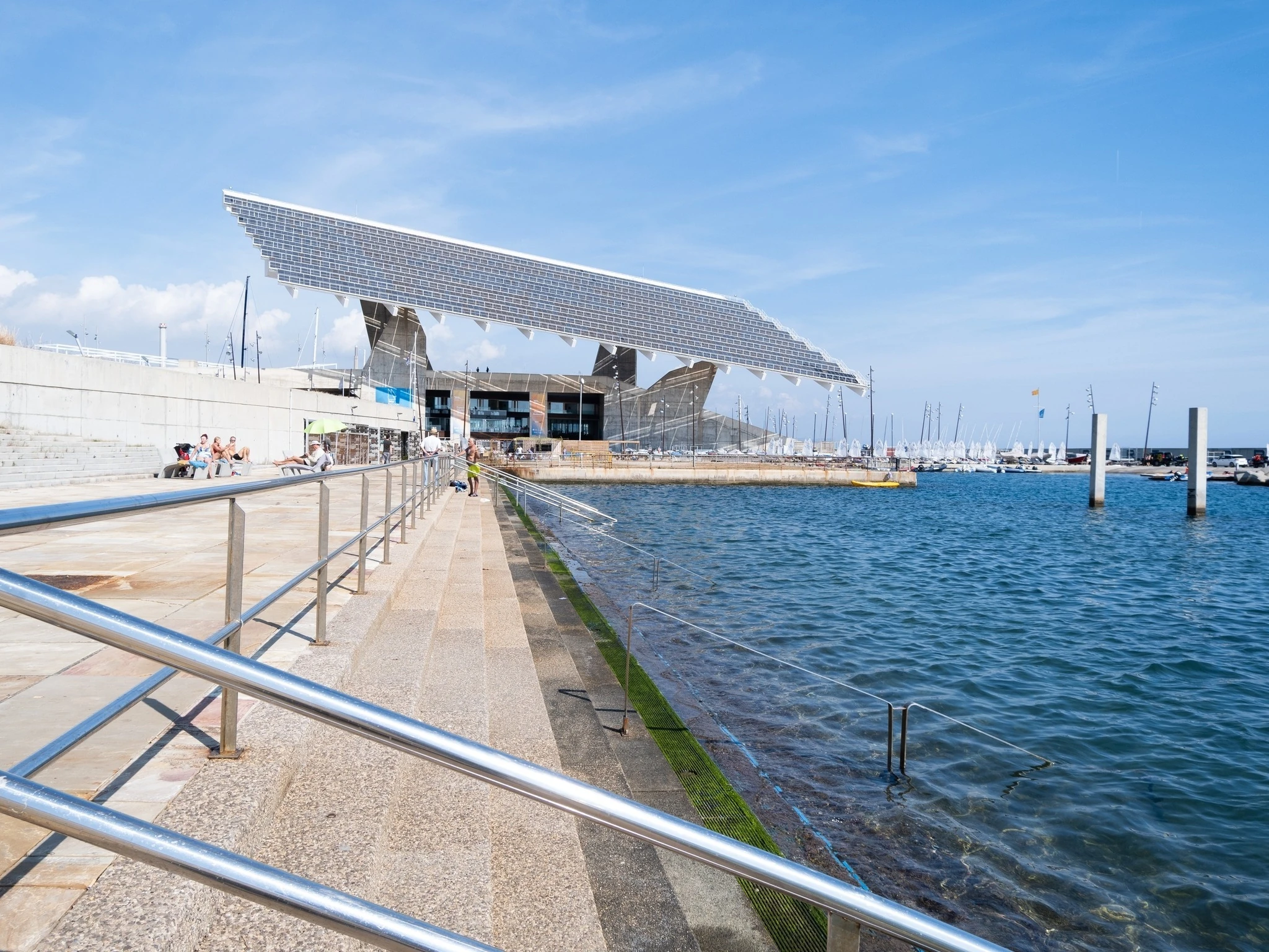 Metal stairs leading to the mediterranean sea and people sun bathing at the Barcelona Forum. Sunny autumn day in Catalonia