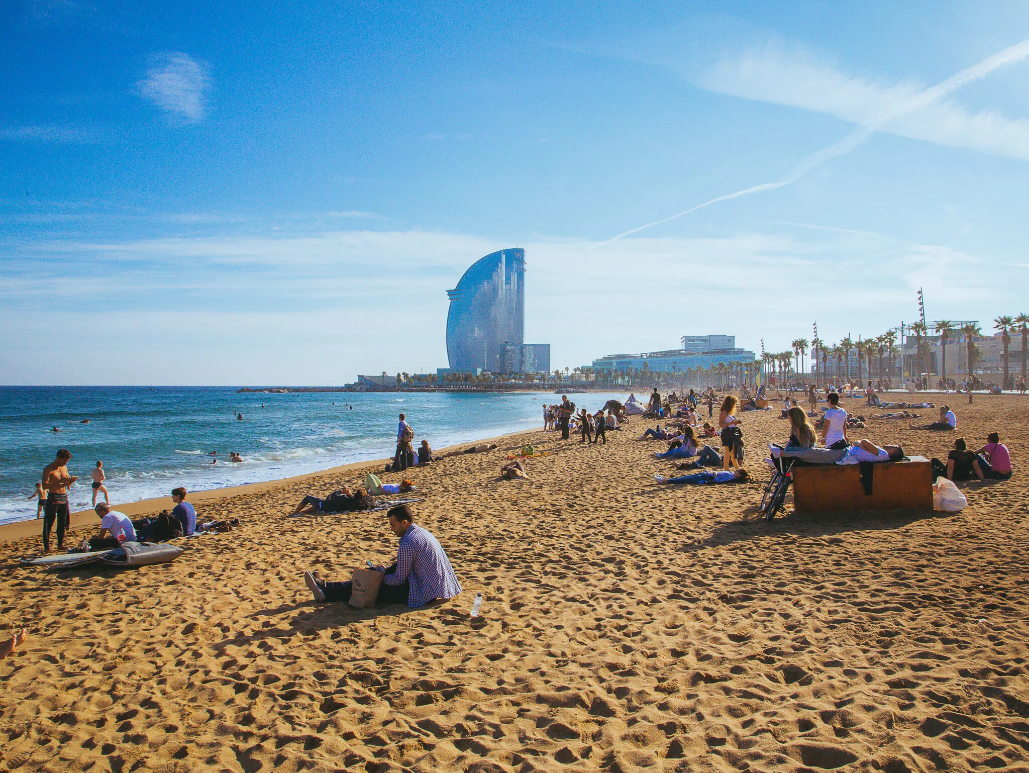 Busy beach in Barcelona with amazing W hotel view on the horizon and people lying on the sand.