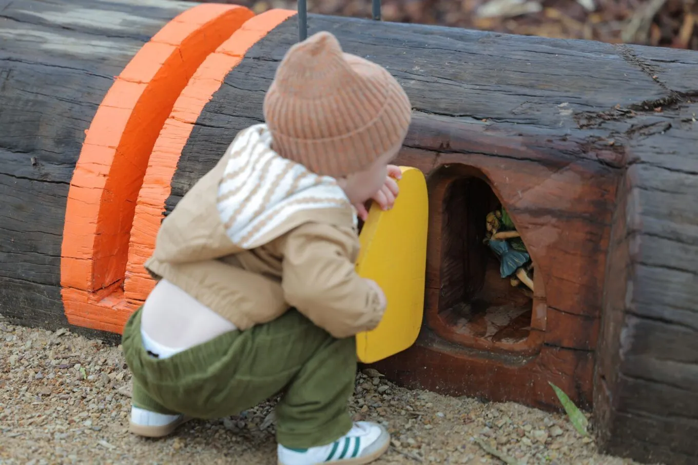 A child looking inside a tiny door to see a fairy figurine.