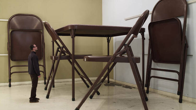 Robert Therrien No title (folding table and chairs, dark brown), 2007 A man looks up at a huge table and folding chairs by Robert Therrien.