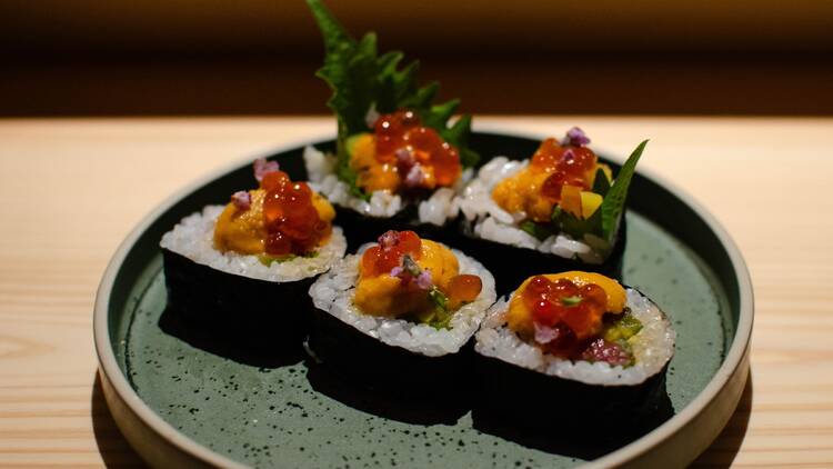 Five sushi rolls on a plate with green garnish sticking out the top