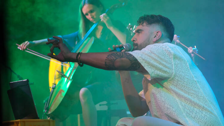 A man on stage with a mic and a woman playing cello 