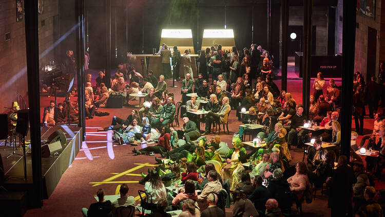 A crowd sitting in front of a stage listening to a musican. 