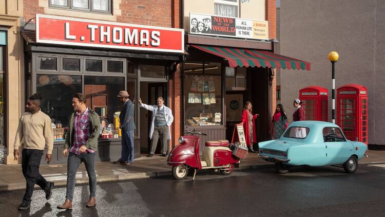 People standing in the street in front of shops and cars set in the 1940's at a living museum