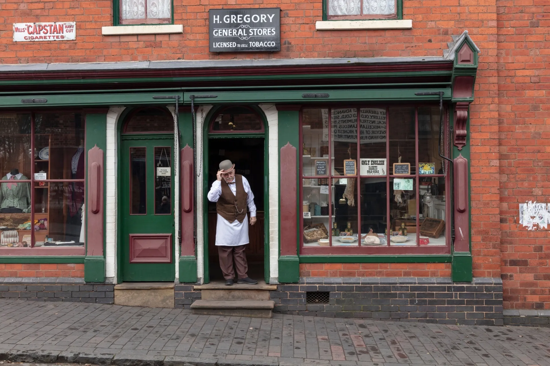 Man standing in the doorway of a general store shop, set in the 1940's at a living museum